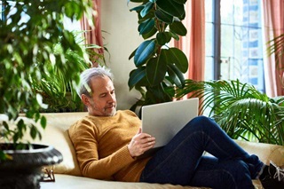Man sitting on couch with computer in front of windows