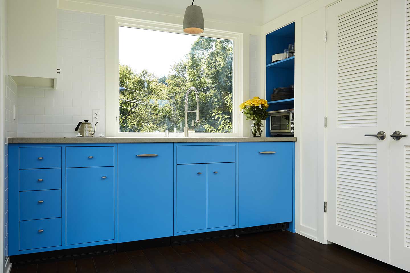 The kitchen inside a contemporary tiny house, with bright blue cabinets below the countertop and a Marvin Ultimate Awning window over the sink.