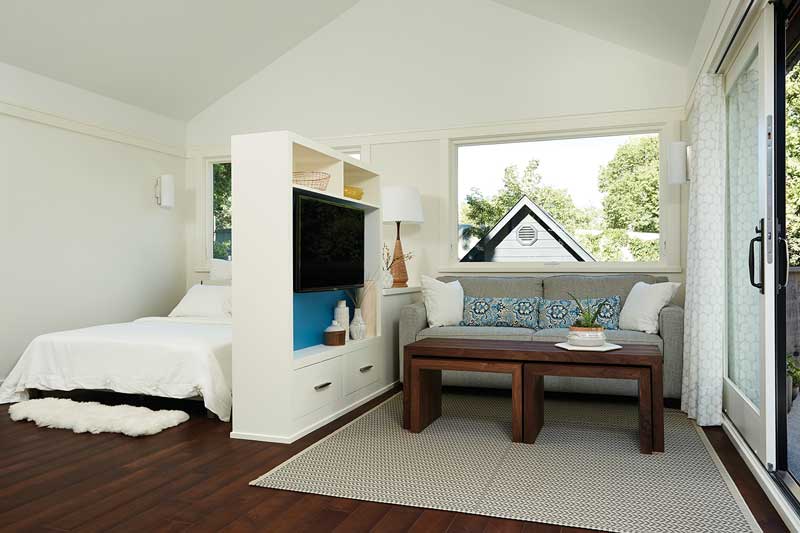 The combined bedroom and living room divided by a TV stand inside a tiny house, featuring Marvin Ultimate Awning windows.
