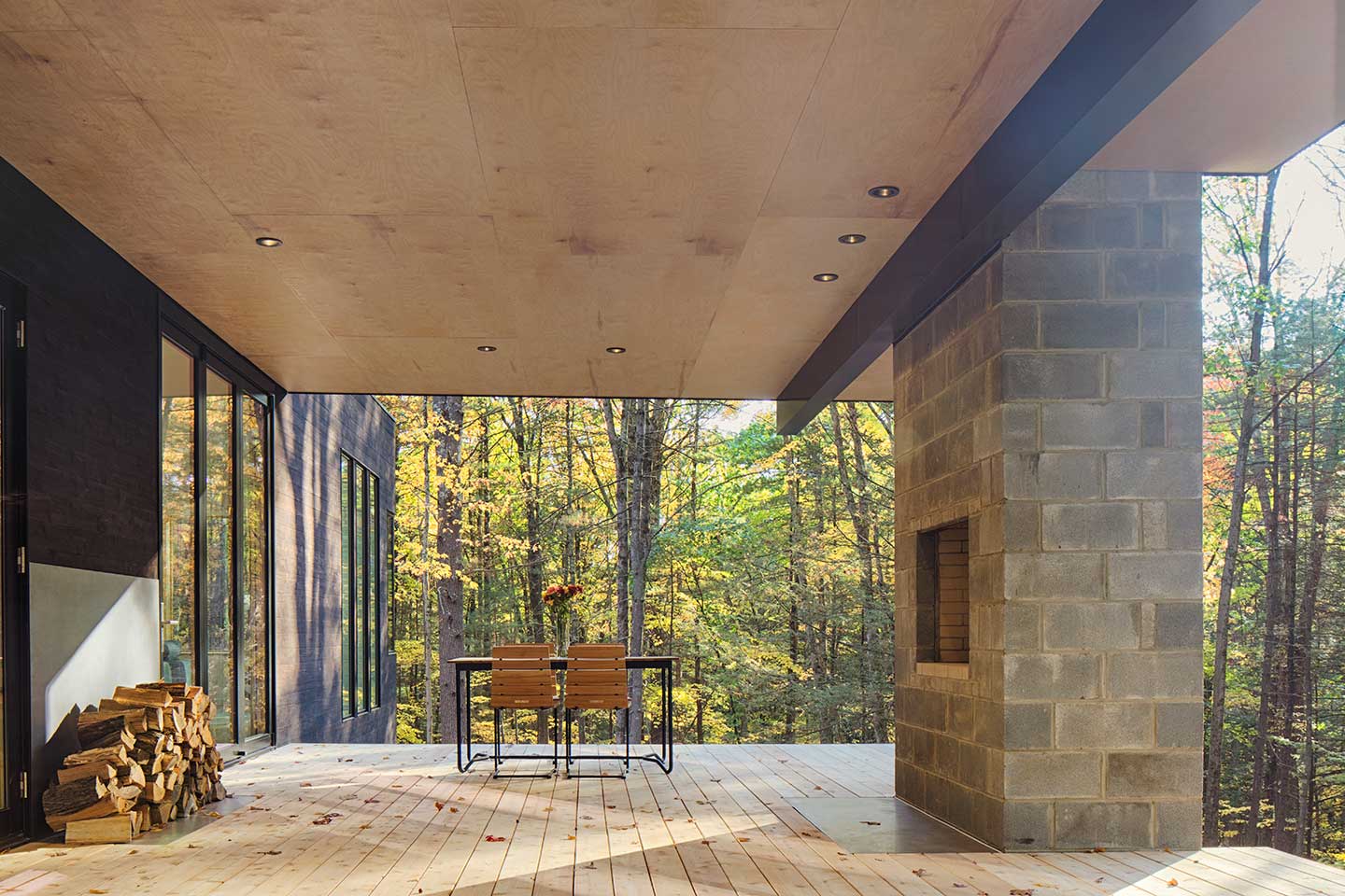 A covered second-story deck with a view of the woods, featuring an outdoor fireplace and Marvin Ultimate Picture windows.