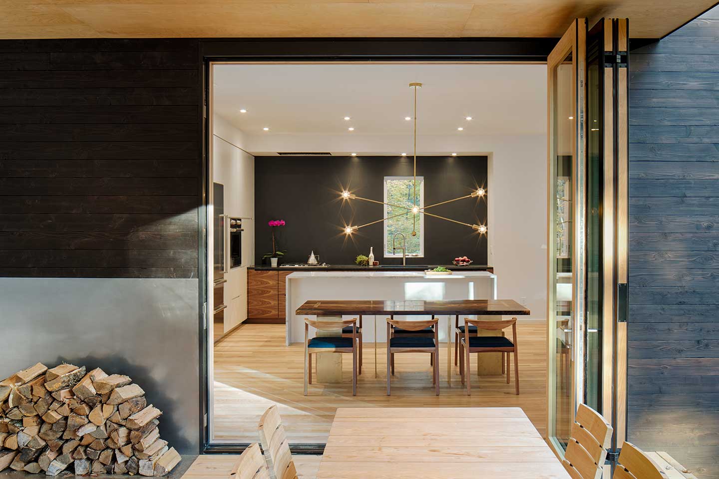 A view from a deck looking into a contemporary kitchen, featuring a black wall with a Marvin Ultimate Casement window.