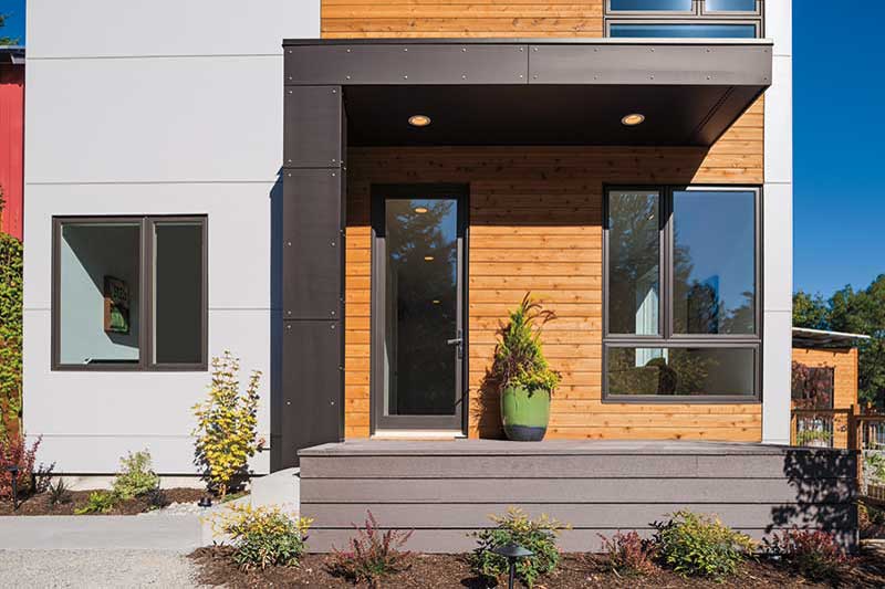A porch at Grow Community featuring a glass Marvin Elevate door next to a large window surrounded by natural wood siding and a black metal clad awning.