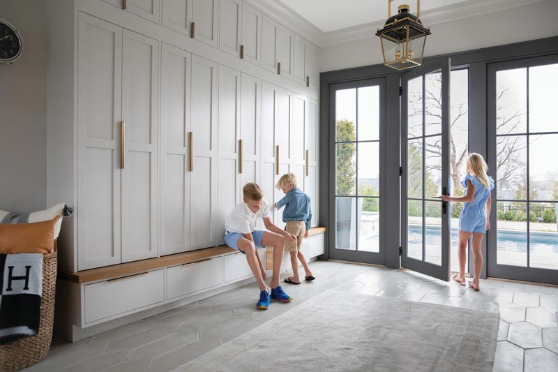 Three children getting their shoes on in a grand mudroom with built-in cabinets and Marvin Elevate Inswing French doors