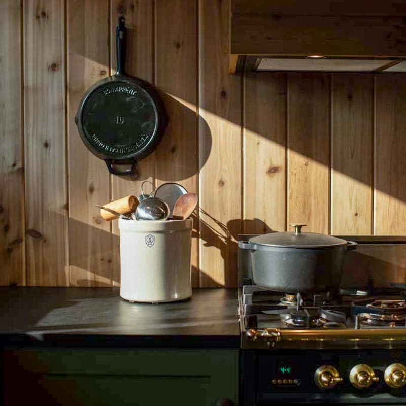 A close up of a cedar-clad wall in the kitchen of a cabin with a cast iron pan hanging on the wall next to the stove.