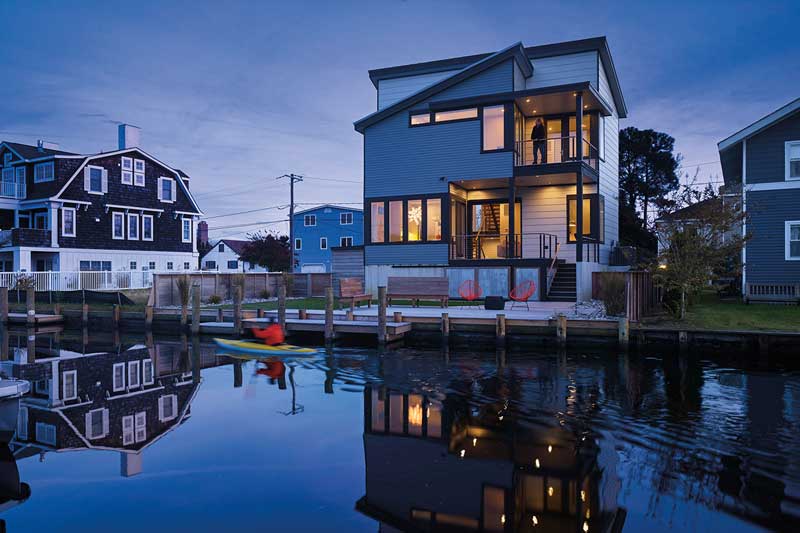 The back of a modern beach house at night on the water, featuring Marvin Elevate Casement windows.