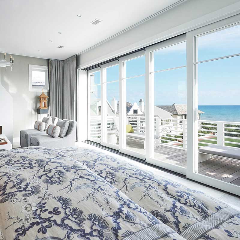 A bedroom with a deck and multi-slide doors overlooking the ocean in Vern Yip’s Rosemary Beach home.