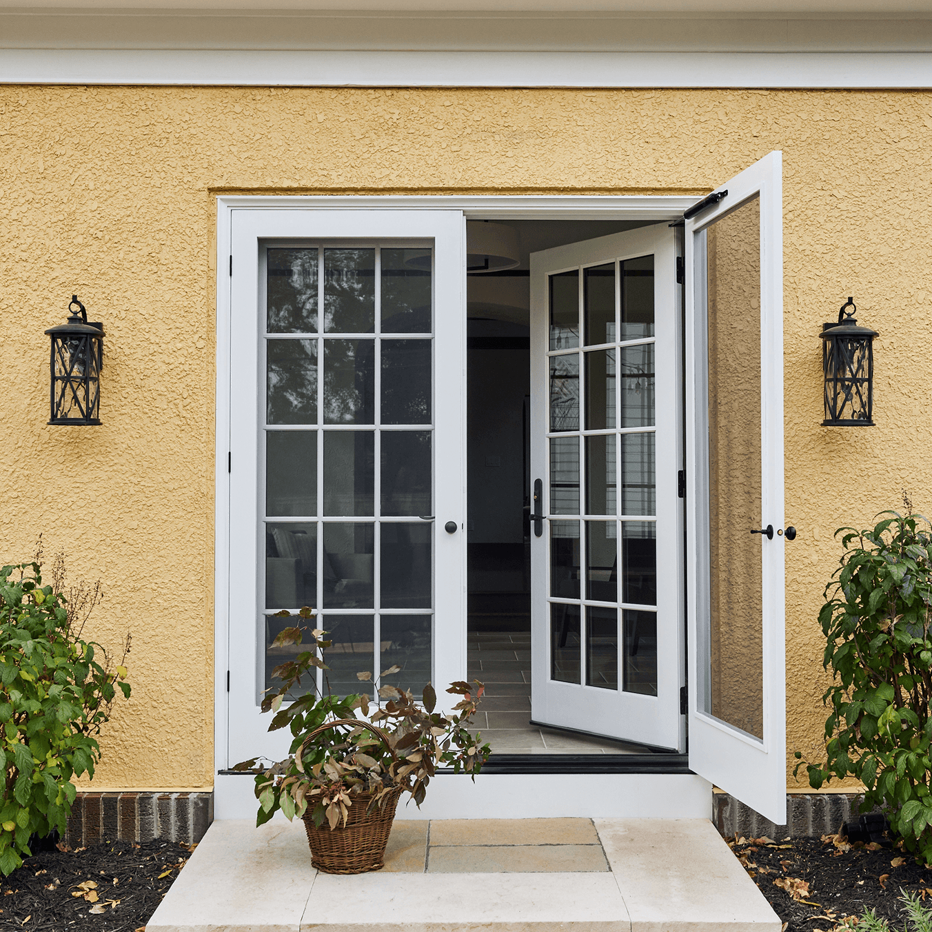 Exterior view of a yellow stucco home with a white opened Marvin Ultimate Wood Inswing French door with divided lites.