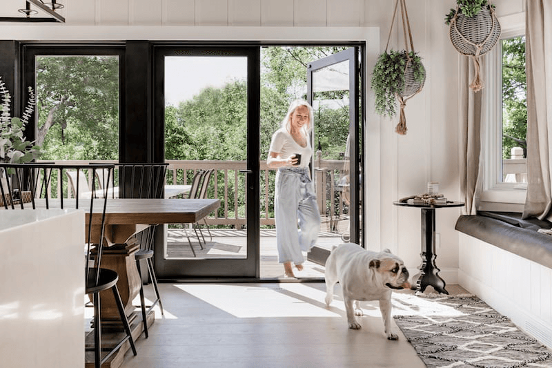 A woman and a white bulldog enter a home through black Marvin Elevate Outswing French Doors.